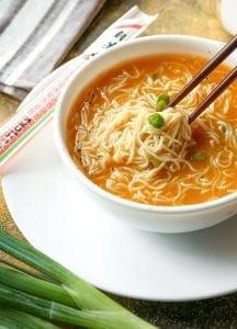 Ramen soup in a bowl with chopsticks removing noodles.