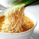 Chopsticks holding noodles above soup.