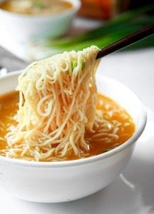 Chopsticks holding noodles above soup.