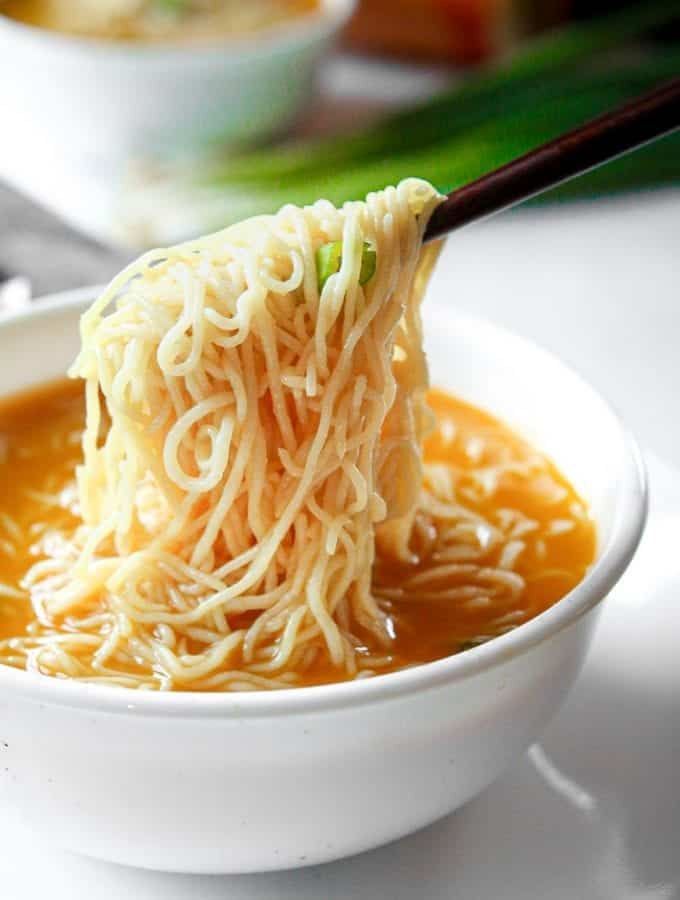 Chopsticks holding noodles above soup.