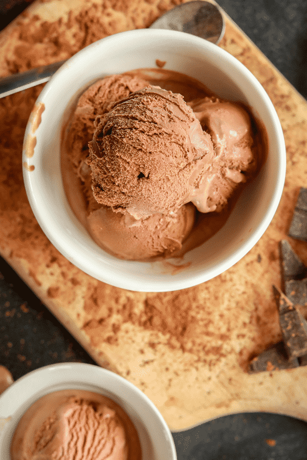 Scoops of chocolate ice cream in a white bowl that is set on top of a cutting board.