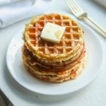 A white plate with a stack of chaffles topped with butter and syrup on it.