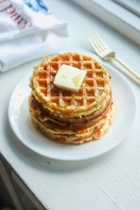 A white plate with a stack of chaffles topped with butter and syrup on it.