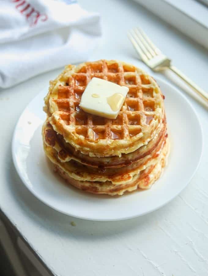 A white plate with a stack of chaffles topped with butter and syrup on it.