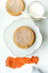A low carb pumpkin spice cookie sitting on a serving plate surrounded by a glass of milk and another cookie.