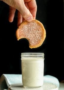 A pumpkin spice cookie with a bite taken out of it about to be dipped in a glass of milk.