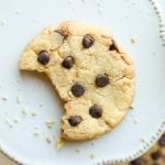 A chocolate chip cookie with a bite taken out of it laying on a plate.