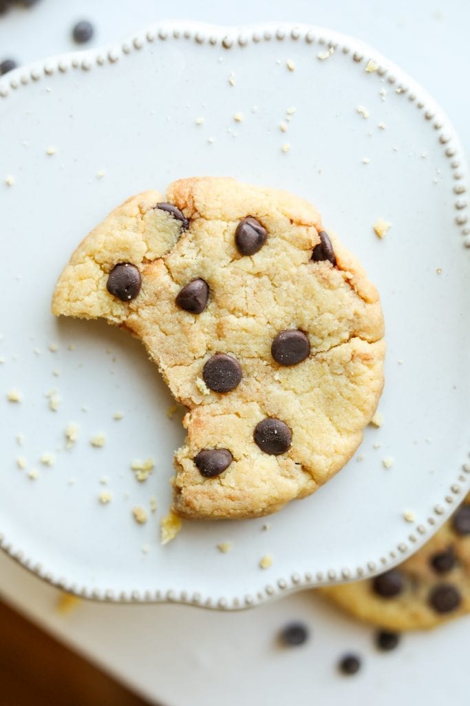 A chocolate chip cookie with a bite taken out of it laying on a plate.