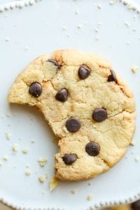 A chocolate chip cookie with a bite taken from it laying on a plate.