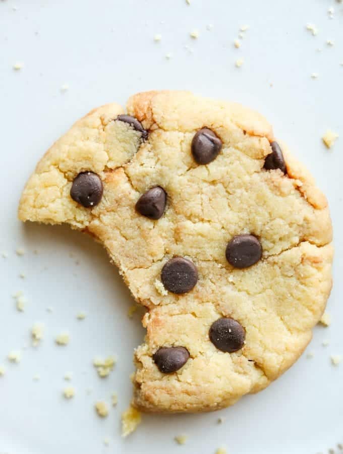 A chocolate chip cookie with a bite taken from it laying on a plate.