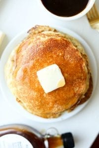 A stack of pancakes on a plate topped with butter and syrup.