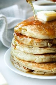 A stack of pancakes on a plate with syrup being poured on them.