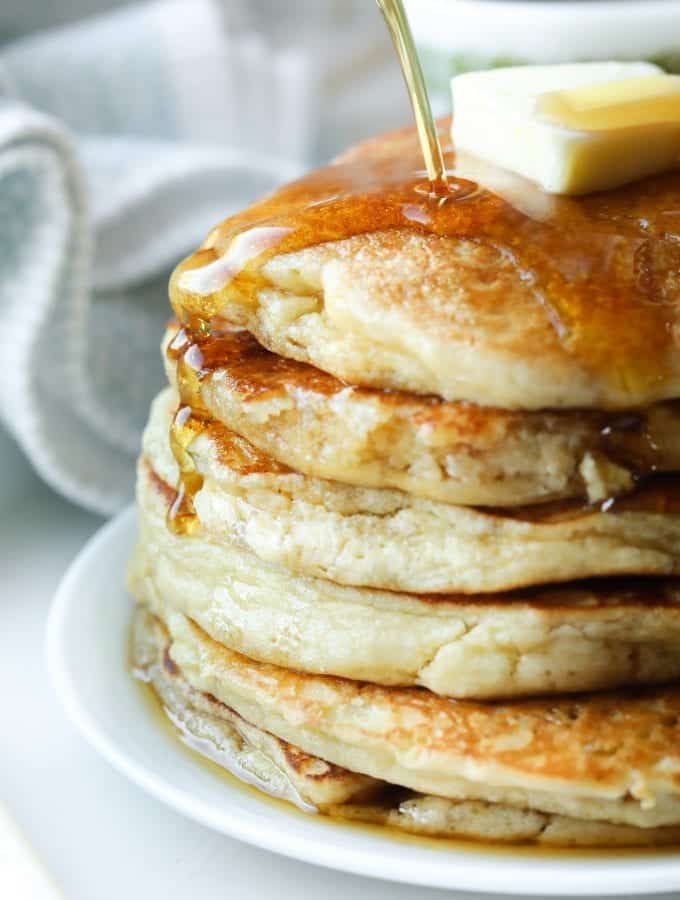 A stack of pancakes on a plate with syrup being poured on them.