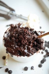 A chocolate lava mug cake sitting on a table sounded by chocolate chips.