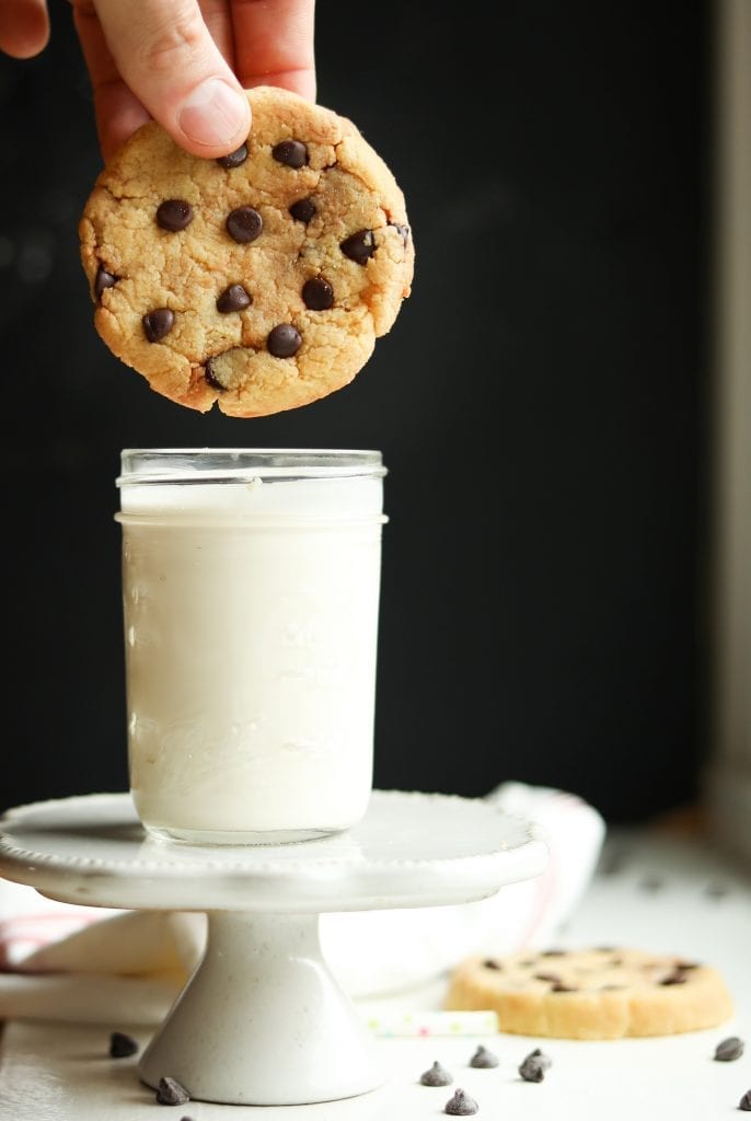 A chocolate chip cookie about to be dipped into milk.