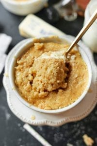 A piece of pancake ready to be eaten. It's scooped on a fork, and set on top of a large pancake made in a mug.