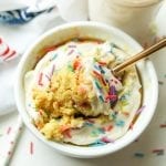 A birthday cake mug cake with a piece about to be removed by a fork.