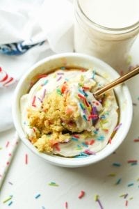 A birthday cake mug cake with a piece about to be removed by a fork.