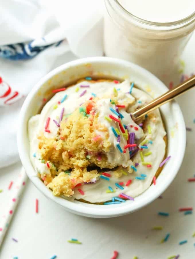 A birthday cake mug cake with a piece about to be removed by a fork.