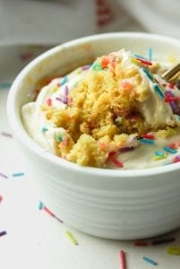 A close up of a birthday cake mug cake with a piece about to be removed from it.