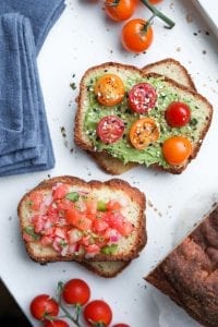 A slice of bread covered with avocado, and another slice covered with salsa.