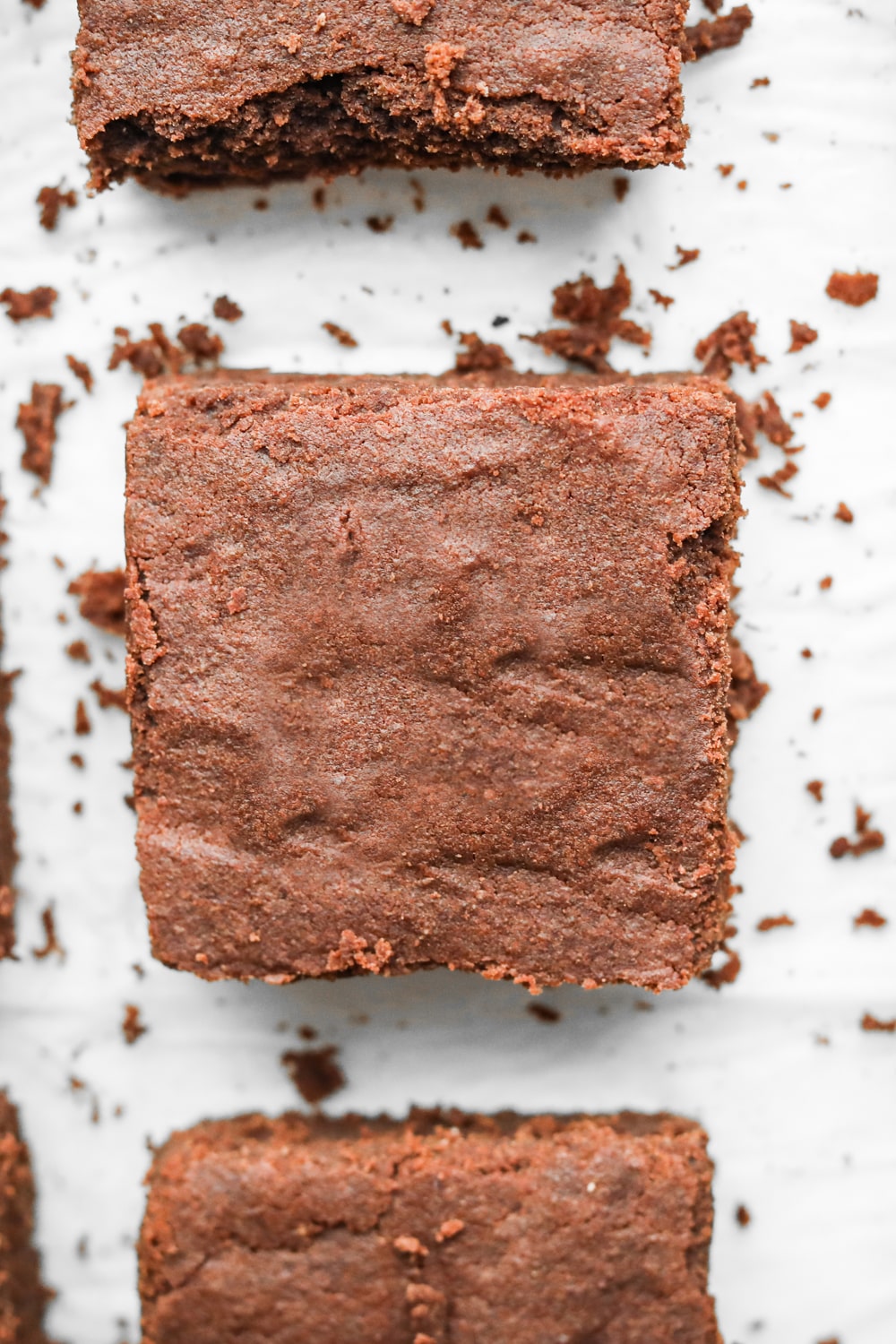 Keto brownies made with coconut flour cut into square laying on parchment paper.