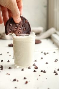 A chocolate keto cookie being dunked in a glass of milk.