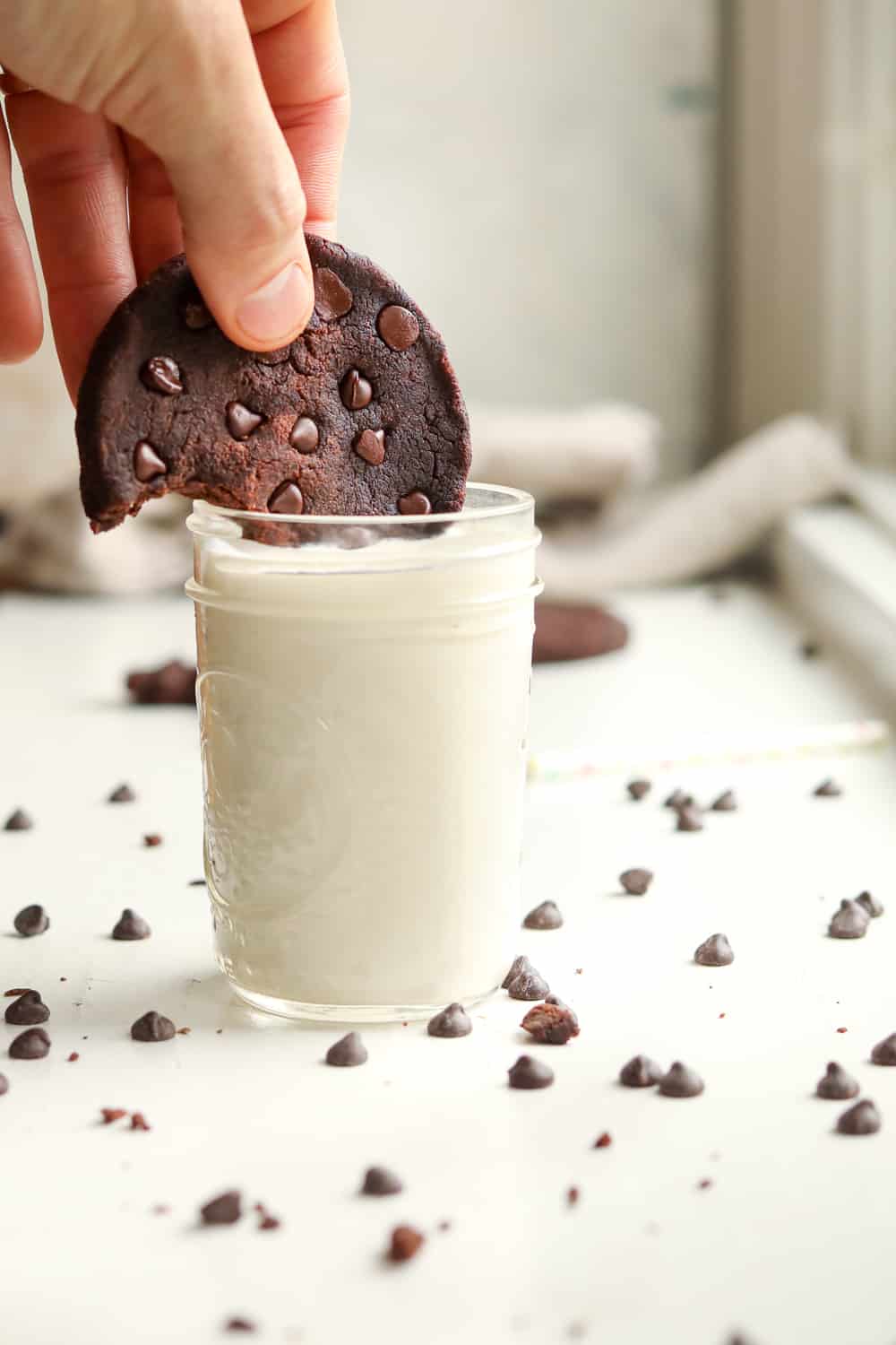 A chocolate keto cookie being dunked in a glass of milk.