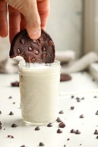 A double chocolate chip cookie that's being removed from a glass of milk.