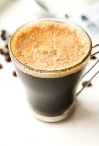 A cup of butter coffee on a table surrounded by coffee beans.