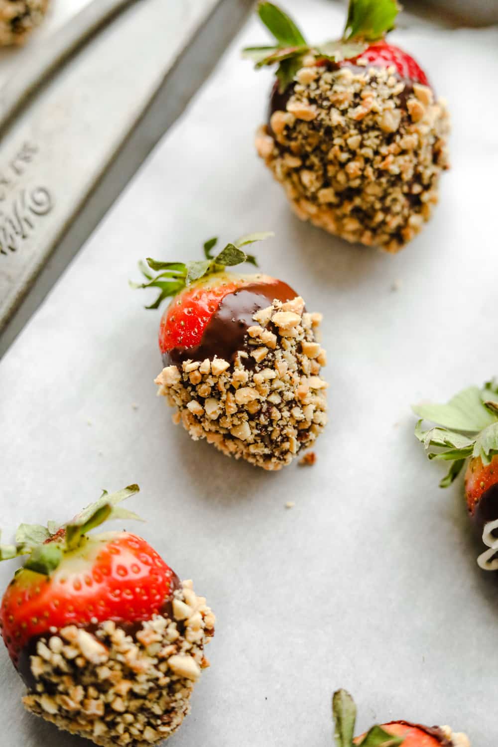 Chocolate covered strawberries dipped in crushed peanuts on a tray.