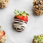 A chocolate covered strawberry with a cream drizzle laying on a tray.