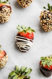 A chocolate covered strawberry with a cream drizzle laying on a tray.