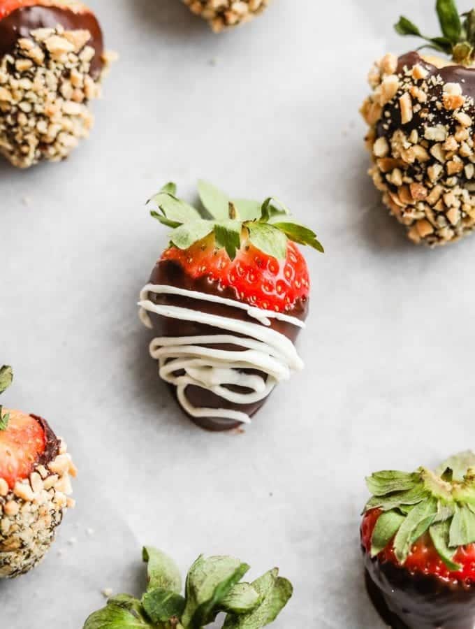 A chocolate covered strawberry with a cream drizzle laying on a tray.