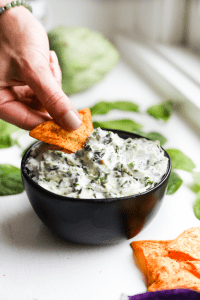 Spinach and artichoke dip being scooped out of a bowl with a chip.