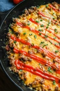 Half of a cheeseburger casserole in a cast iron pan topped with chives and keto ketchup.