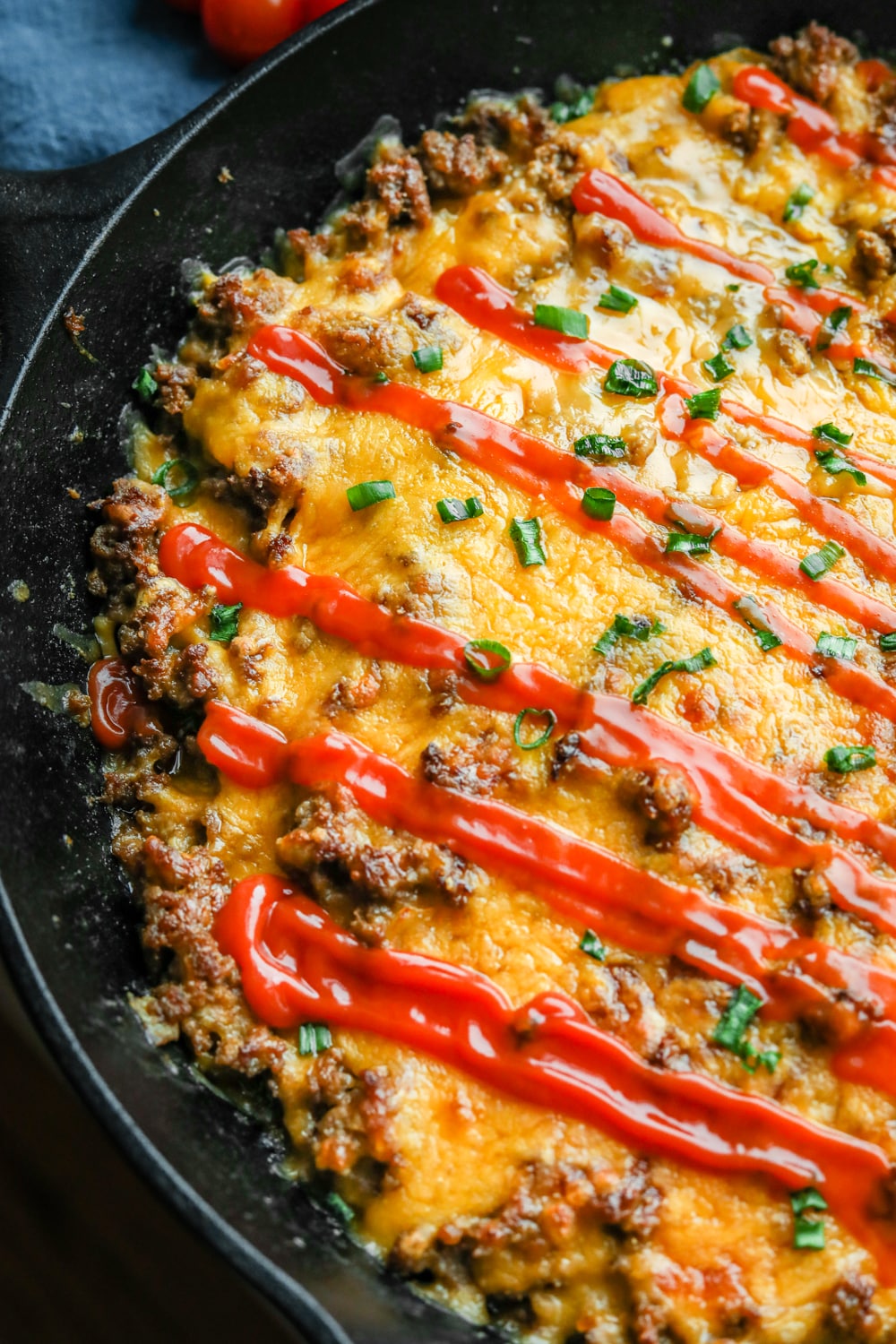 Half of a cheeseburger casserole in a cast iron pan topped with chives and keto ketchup. 