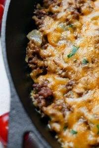 The edge of a pan with filled with ground beef, onions, and topped with cheddar cheese and chives.
