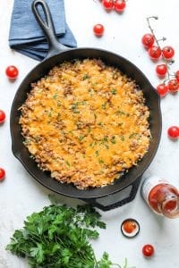 A keto cheeseburger casserole surrounded by tomatoes and low carb ketchup.