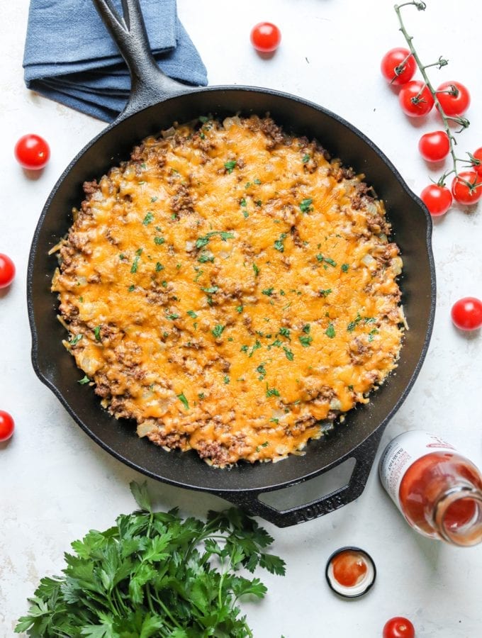 A keto cheeseburger casserole surrounded by tomatoes and low carb ketchup.