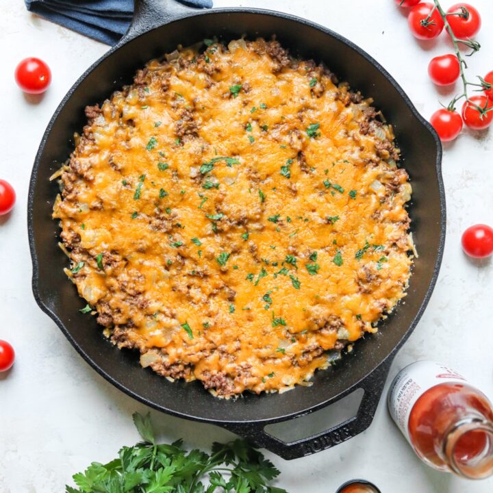 A keto cheeseburger casserole surrounded by tomatoes and low carb ketchup.