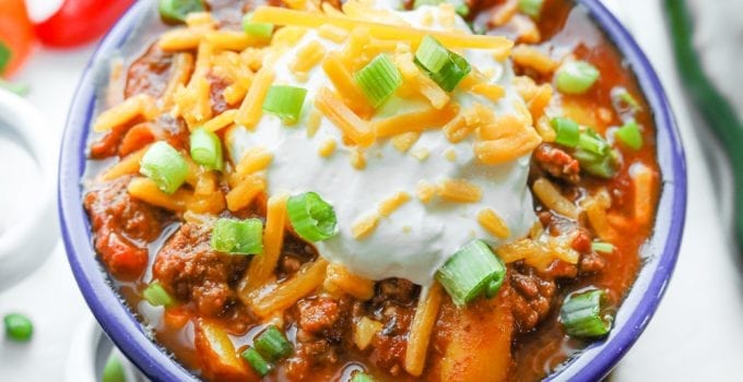 A bowl of keto chili surrounded by tomatoes and peppers.