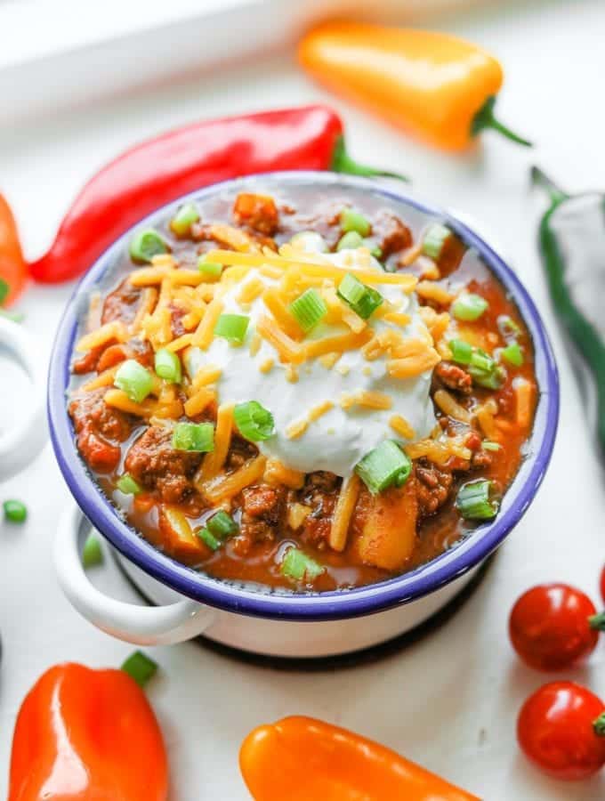 A bowl of keto chili surrounded by tomatoes and peppers.