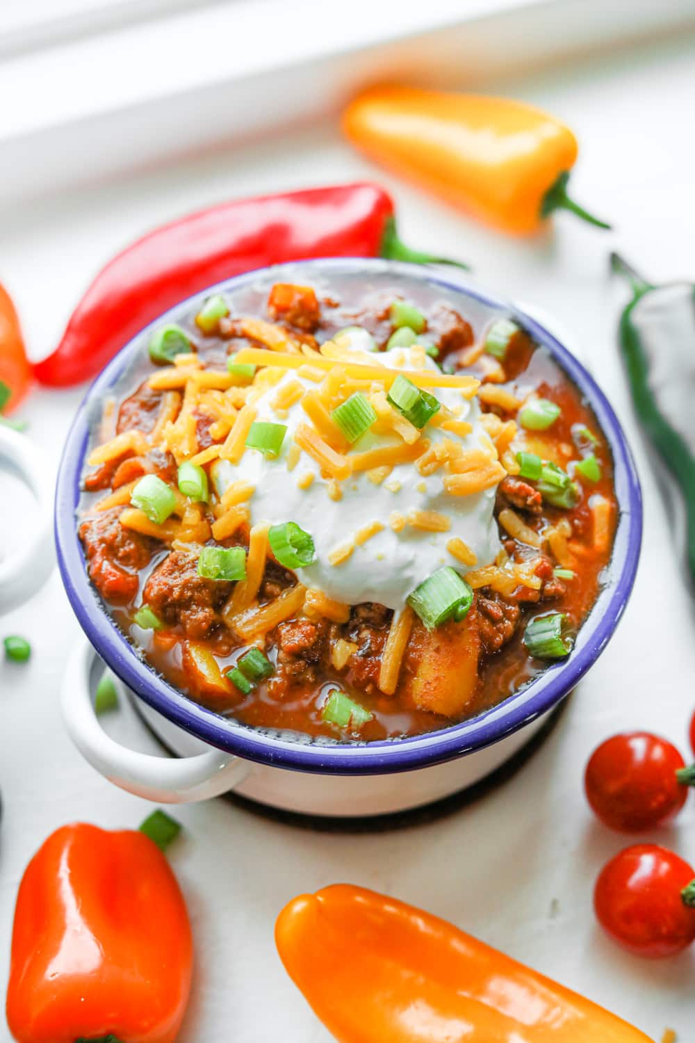 A bowl of keto chili surrounded by tomatoes and peppers.