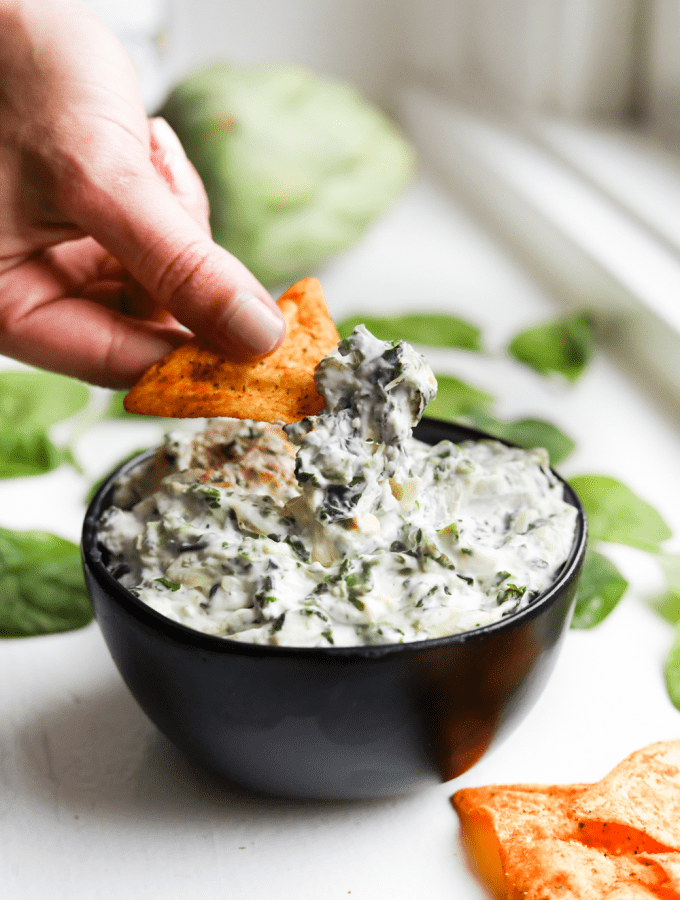 Spinach and Artichoke dip being scooped out a bowl with a low carb chip.