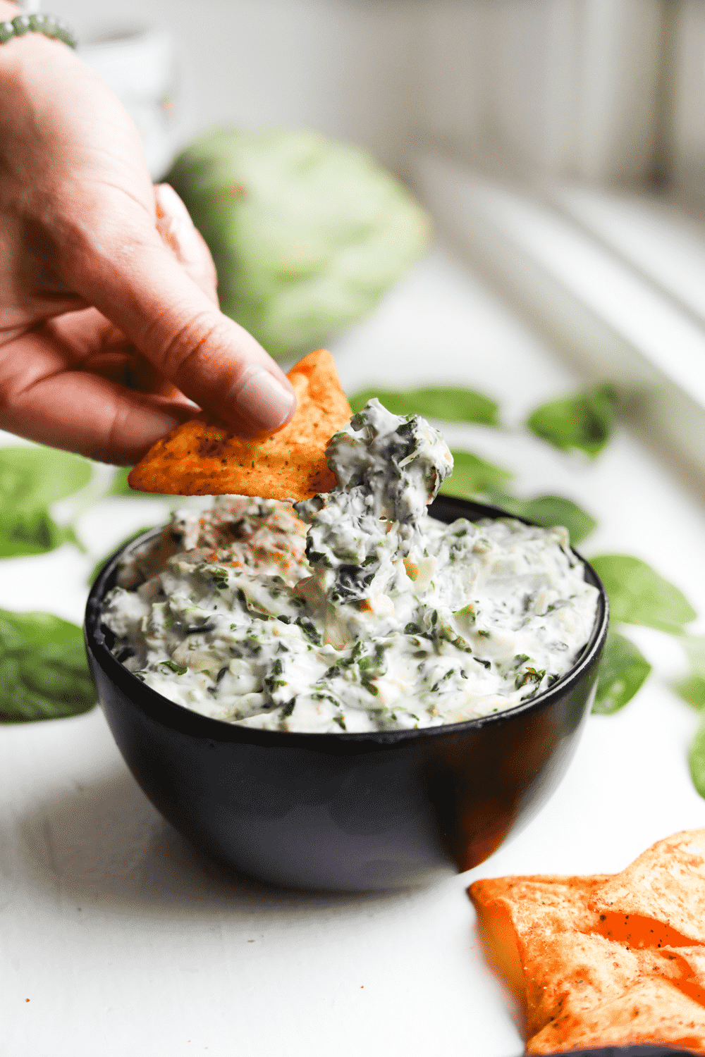 A chip being dipped into a bowl of keto spinach an artichoke dip