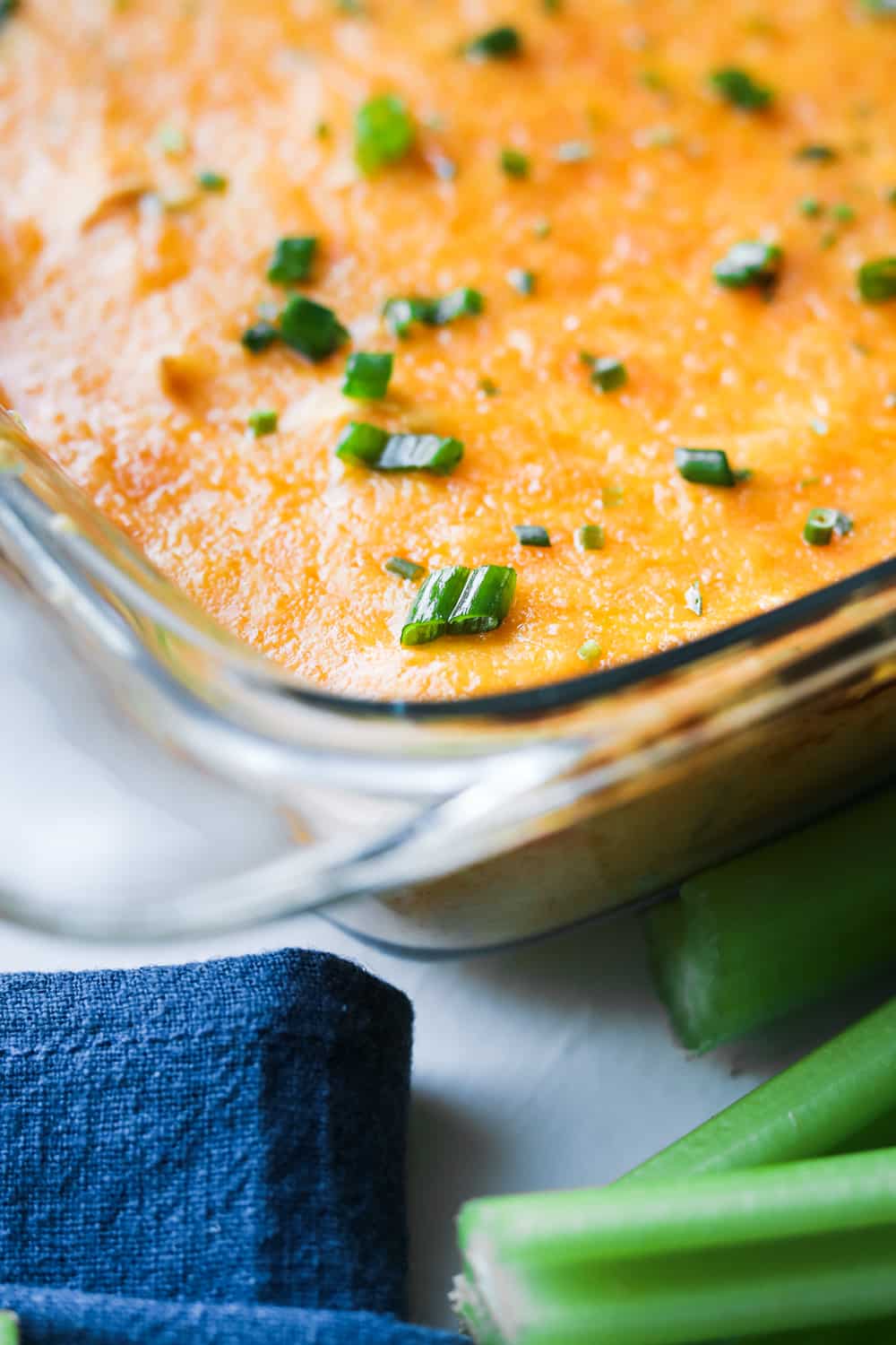 Buffalo wing dip in a dish surrounded by sticks of celery.