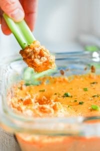 Keto Buffalo chicken wing dip being scooped out of a dish with a piece of celery.
