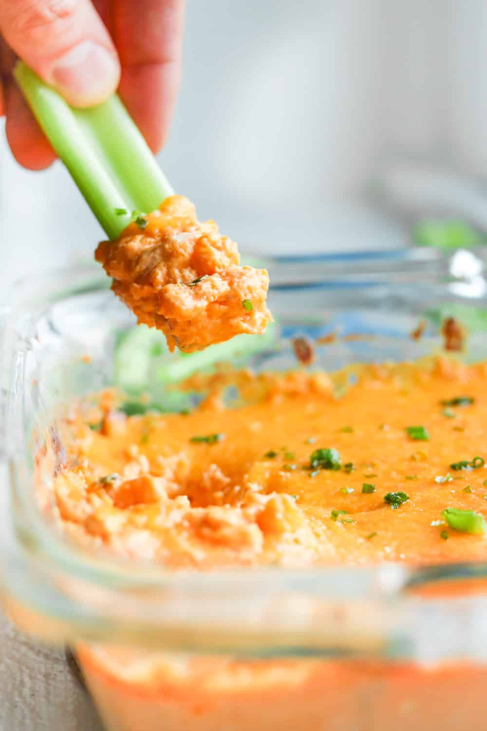 Keto Buffalo chicken wing dip being scooped out of a dish with a piece of celery.