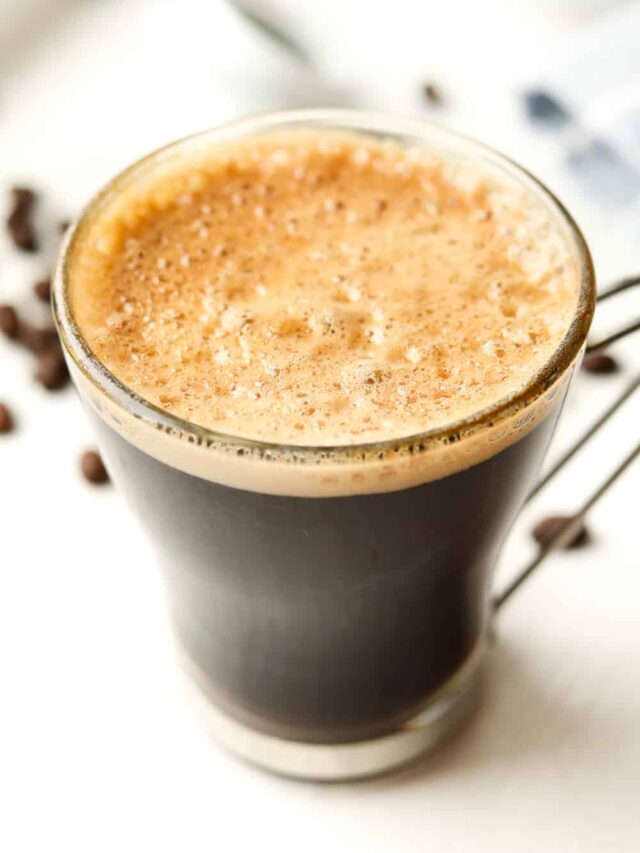 A cup of butter coffee on a table surrounded by coffee beans.